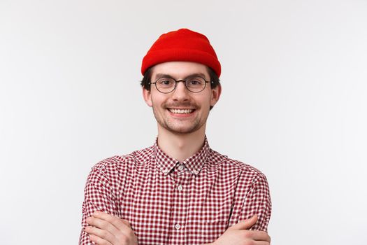 Close-up portrait of confident cheerful young man expressing himself with bright outfit, wear hipster red beanie and checked shirt, cross hands on chest like pro, smiling delighted, white background.