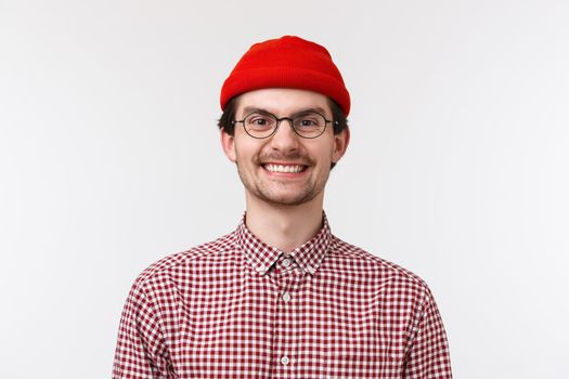 Close-up portrait cheerful funny young man with beard and moustache, smiling delighted white teeth perfect smile, wear glasses and red beanie, standing white background upbeat, positive emotions.