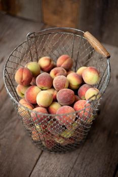 Fresh peaches fruits in basket on dark wooden rustic background, top view. Summer harvest of fruit. Still life. A group of ripe peach. Flat lay vegan food. Copy space.