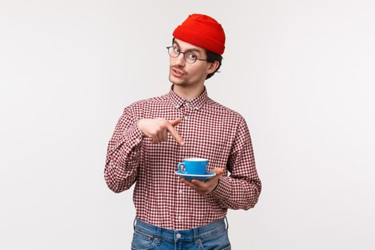 Want some. Friendly-looking funny young hipster bearded guy in red beanie and glasses, suggest coworker cup of coffee, pointing at his tea as asking for refill, standing white background.