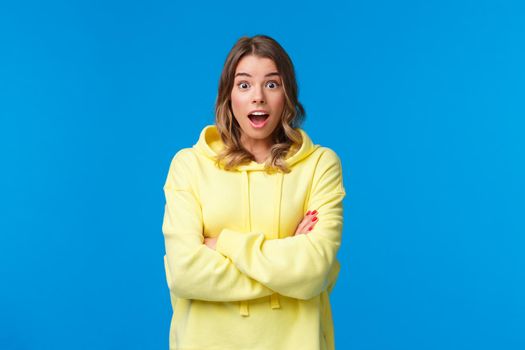 Really omg. Impressed and surprised blond woman react astonished listening stunning shocking story, open mouth and look camera with amazement, cross hands chest casual pose over blue background.