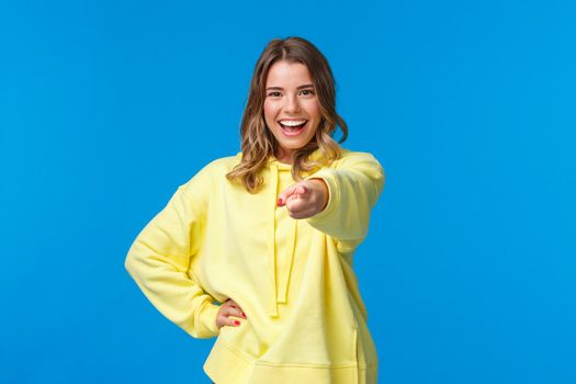 I choose you. Confident and cool young blond hipster girl with short haircut, yellow hoodie, pointing finger at camera with self-assured expression making final choice, inviting join team.