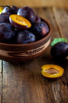 Blue plum in a bowl on a wooden table. Plums in a cut. Top view, place for text. Fruit background with copy space.