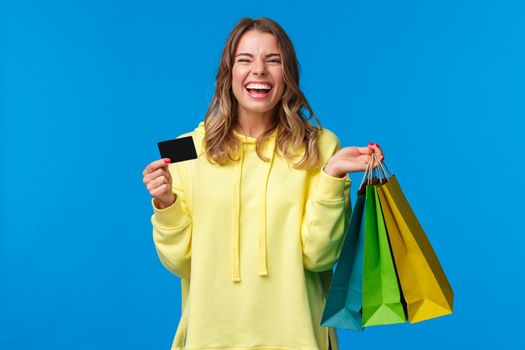 Carefree emotive, smiling happy pretty blond girl using credit card to waste some money in mall, holding shopping bags, buy gifts or presents, treat yourself day, laughing joyfully.