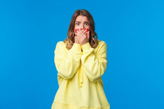 Shocked speechless and concerned young woman seeing bad accident, terrifying scene in movie, cover mouth with hands not to scream, stare with frightened eyes camera.