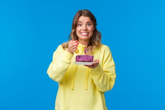 Celebration, party and lifestyle concept. Cute silly blond girl worry as trying think what she wants to wish while blowing out candle on b-day cake, smiling awkward, celebrate birthday.