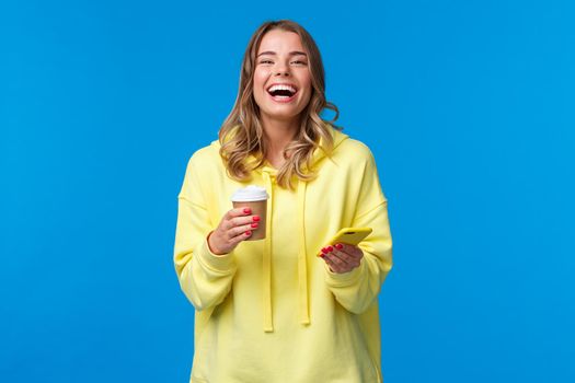Conversation, people and emotions concept. Joyful pretty blond woman talking to friends laughing over jokes as drinking take-away coffee from paper cup, holding smartphone.