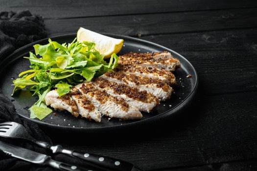 Crumbed, chicken breast fillet grilled, over black wooden table with space for text