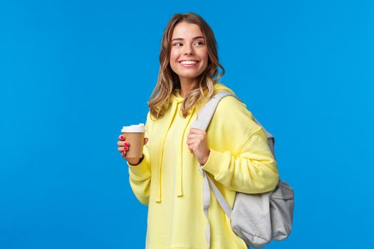 Lifestyle, college and people concept. Good-looking carefree blond woman going university look around happy and pleased smiling as drinking take-away coffee and holding backpack.