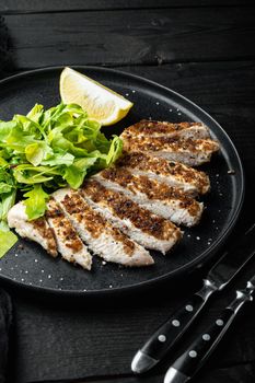 Crumbed, chicken breast fillet grilled, over black wooden table