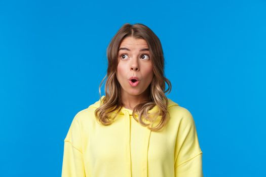 Wow amazing, really incredible news. Astonished young european female with short blond hair react to wonderful interesting event going nearby, standing blue background intrigued.