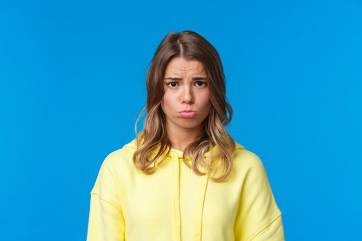 Close-up portrait cute gloomy and upset sulky blond girl with short haircut, sobbing and pouting frowning distressed, offended being rejected or let down, standing blue background.