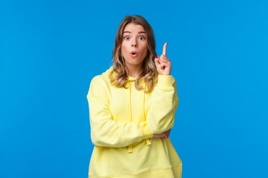 Got an idea. Excited creative and smart blond caucasian woman have suggestion, show eureka gesture with index finger raised up, talking to team, made-up plan, stand blue background.