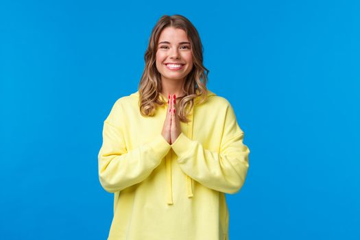 Cheerful young european female practice yoga, greeting sensei with namaste gesture, hold hands in pray and smiling grateful with relaxed carefree expression, smiling camera, blue background.