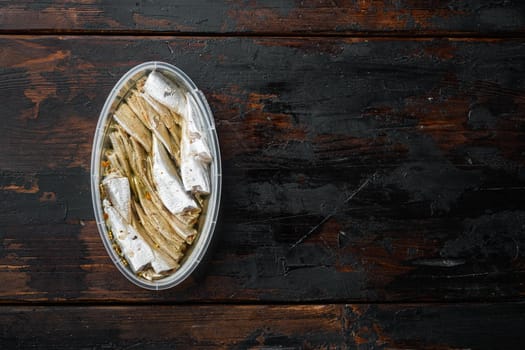 Salted anchovy fillets set, in plastic container, on old dark wooden table background, top view flat lay, with copyspace and space for text