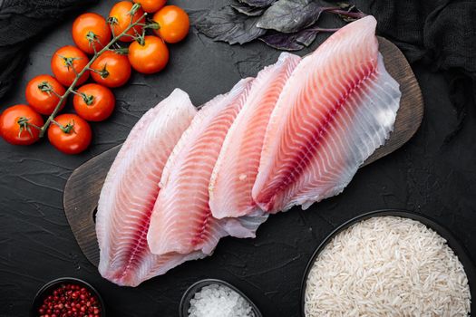 White fish fillet, with basmati rice and cherry tomatoes ingredients, on black background, top view