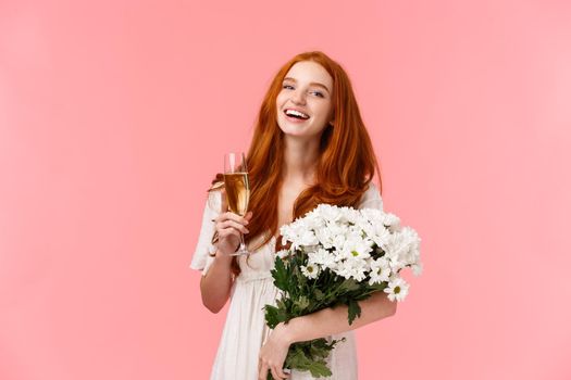 Attractive, cheerful b-day girl with red curly hair, laughing and looking camera carefree as speaking to friends during party, birthday celebration, holding bouquet white flowers and champagne glass.