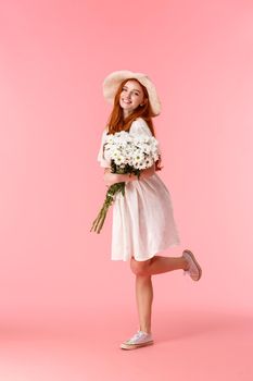 Full-length vertical shot happy, cheerful attractive woman with red long hair, straw hat, wearing cute summer white dress, dancing, heading home from romantic date with flowers, holding bouquet.