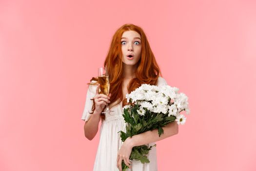 Surprised and astonished, curious redhead girl staring speechless and amazed and friend congratulating her and bring amazing awesome gift, holding bouquet flowers and glass champagne.