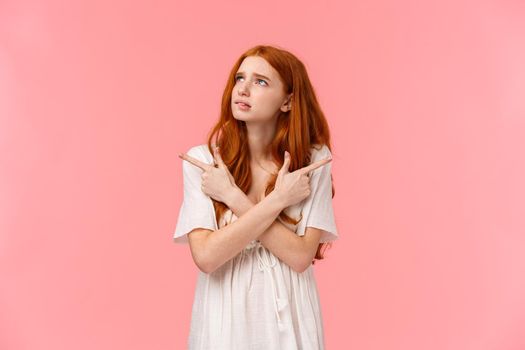 Decisions are so tough. Girl stumble upon hard choice in her life, biting lip nervously, look upper left corner, trying decide, choosing from two products, pointing sideways, pink background.