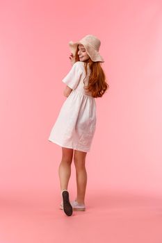 Full-length vertical shot upbeat, charismatic and cute, silly redhead female in white dress and summer straw hat, walking along beautiful park, enjoying vacation, turn back to smile camera coquettish.