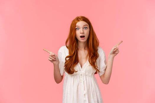 Fascinated and questioned cute redhead woman asking question about interesting advertisements, curious about cool promos, pointing fingers left and right, staring impressed camera.