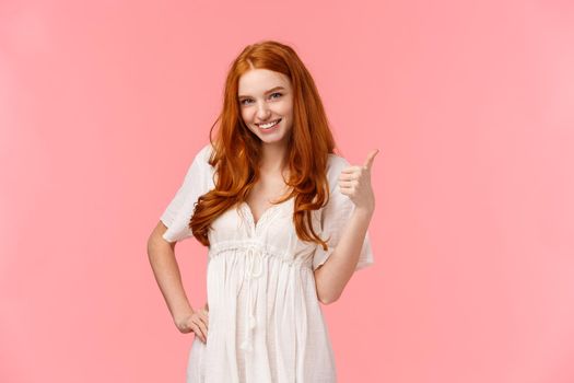 Satisfaction, advertising and lifestyle concept. Cheerful happy and pleased redhead female in white stylish dress, show thumb-up in like gesture, approve choice, satisfied with good decision.