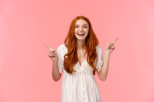 Waist-up portrait happy excited, redhead female in white dress, laughing happily, pleased with both products, introduce variants, pointing sideways, left and right, standing pink background.