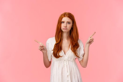 Upset, pouting and gloomy silly redhead female in white dress, whining, telling about bad experience, pointing fingers upper right and left corners, two variants both didnt fit, pink background.