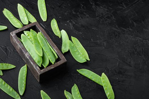 Sugar snap peas, raw ripe baby pods set, in wooden box, on black stone background , with copyspace and space for text