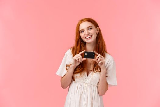 Waist-up portrait, cute and fashionable redhead female in lovely white dress, holding credit card and smiling, ready for shopping, going in store, making internet purchase, place money on deposit.
