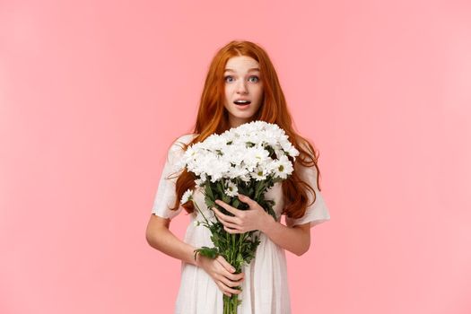 Birthday, celebration and valentines day concept. Surprised romantic and alluring redhead lovely girlfriend receive gift of beautiful white flowers, embracing bouquet and looking touched.