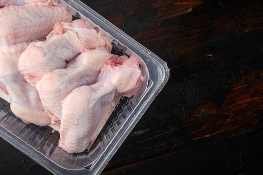 Fresh chicken wings spit in plastic vacuum pack set, on old dark wooden table background, top view flat lay, with copy space for text
