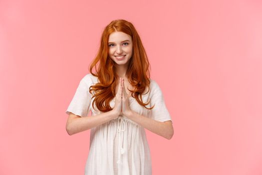 Lovely grateful redhead girl thanking for help, express gratitude, smiling happy, press hands together in namaste, pray gesture, standing pink background, appreciate effort, pink background.