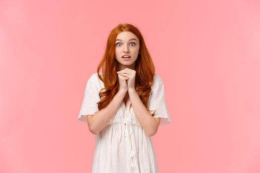 Hopeful and amused, redhead female in white dress, holding hands together over chest in praying pose, glancing camera nervously anticipate important news, seeing something heartwarming.