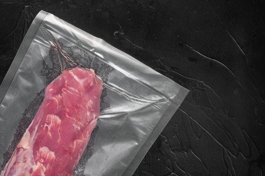 Vacuum packaging of meat products pork fillet tenderloin set, on black stone background, top view flat lay , with copyspace and space for text