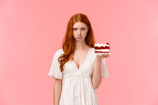 Waist-up portrait upset, uneasy and gloomy cute birthday girl feeling unhappy, sighing, pouting and looking camera distressed, holding peace cake on plate unsatisfied with bad party, pink background.