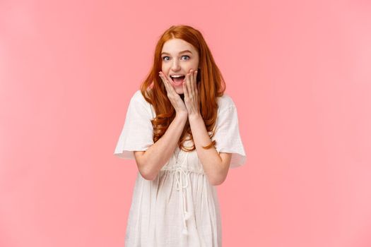 Expectation, anticipation and happiness concept. Amused cute redhead silly girl looking surprised and excited, gasping fascinated, looking charmed and amazed camera, pink background.
