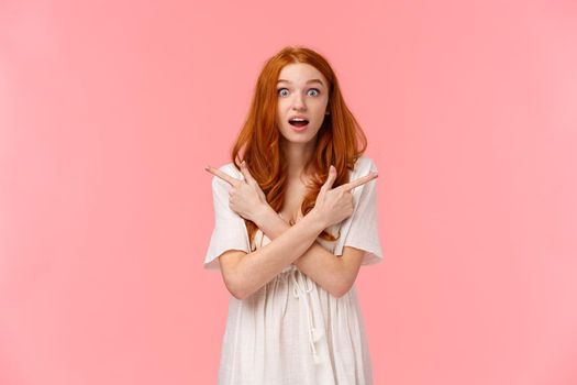 Excited and amused, curious redhead female shopaholic cant make final choice, have two variants, asking help with decision, interested in your opinion, pointing fingers left and right look thrilled.