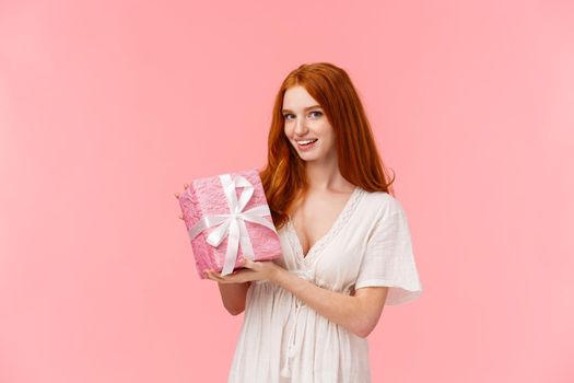 Waist-up portrait charming, romantic and feminine redhead girlfriend in white dress, prepared cute gift. wrapped present in paper and smiling camera, congratulating friend with birthday.