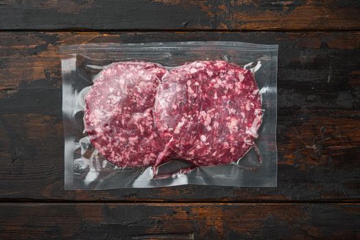 Beef patties in a vacuum packing set, on old dark wooden table background, top view flat lay