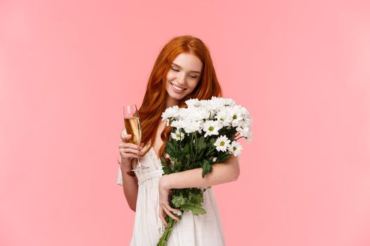 Lovely, sensual and feminine redhead woman holding beautiful bouquet of flowers, sighing and smiling touched, drinking champagne from glass, celebrating valentines day, attend romantic date.