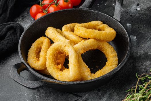 Oven baked breaded calamari rings set on cast iron frying pan skillet, on black dark stone table background