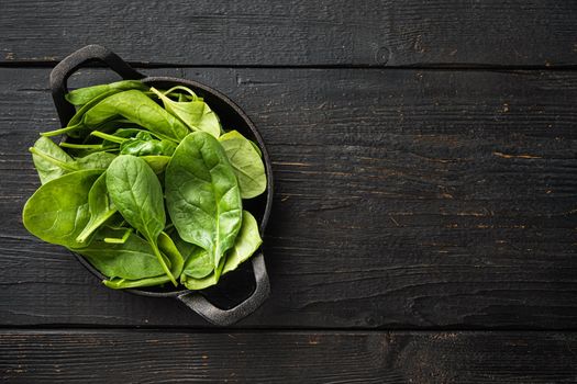 Bundle of fresh spinach set, in frying cast iron pan or pot, on black wooden table background, top view flat lay, with copy space for text