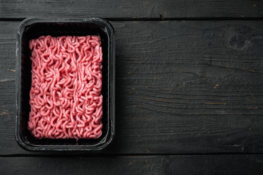 Ground beef meat in plastic tray set, on black wooden table background, top view, flat lay, with copy space for text