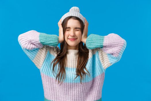Dont want hear it. Waist-up portrait brunette girl unwilling hear anything, standing near loud company, shut ears with hands, close eyes squinting discomfort, wear winter clothes, blue background.