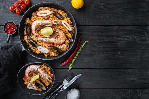 Valenciana seafood paella in bowl and frying pan on black wooden planks, top view with space for text, food photo.