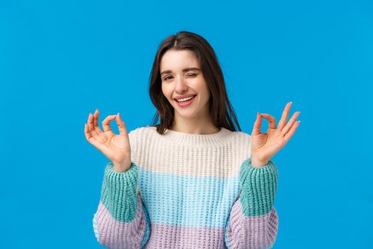 Dont worry everything alright. Relaxed and chill good-looking assertive young woman in winter sweater, wink and smiling assuring all okay, showing ok gestures satisfied, give approval.