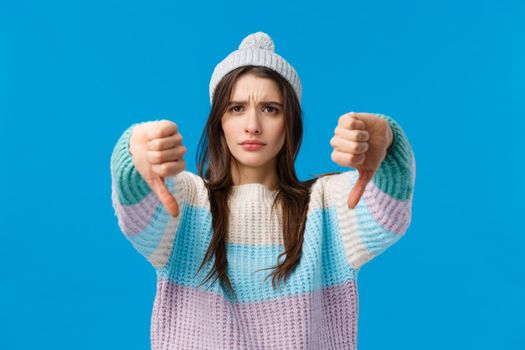 Bad idea, dont do it. Serious-looking upset and angry young woman in winter sweater, hat, looking with judgement, skeptical make thumbs-down gesture, disagree dislike something, give refusal.