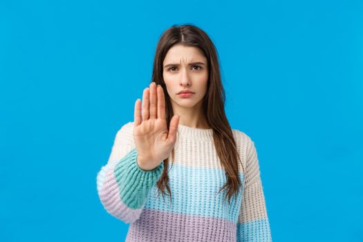 Quit it, enough. Displeased serious and fed up young assertive girl, showing stop gesture, raise palm and frowning disapproval, refuse, prohibit and disagree, standing blue background.
